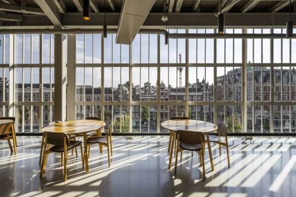 Zitgedeelte met houten tafels en stoelen in een modern interieur met uitzicht op de Sint-Jorissteeg en historische panden in Amsterdam.